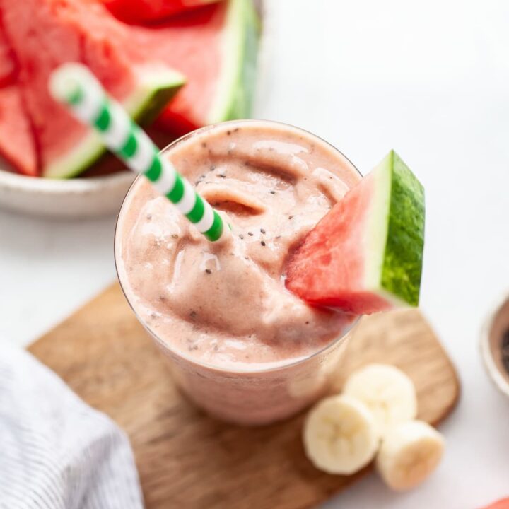 glass of watermelon banana smoothie with a green straw and a piece of watermelon as a garnish