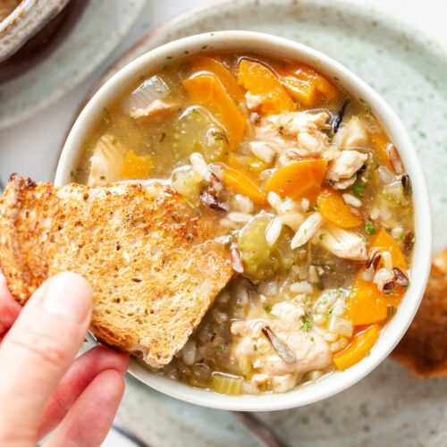 image of instant pot chicken rice soup in a bowl with bread being dipped into the bowl