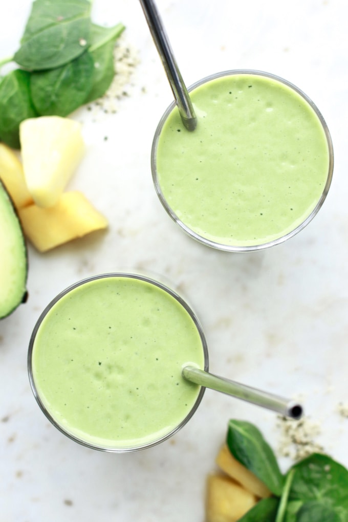 Two healthy green smoothies in glass cups with reusables straws