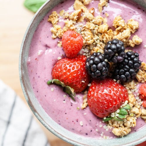 close up of a berry smoothie bowl topped with fresh strawberries, blackberries, and granola