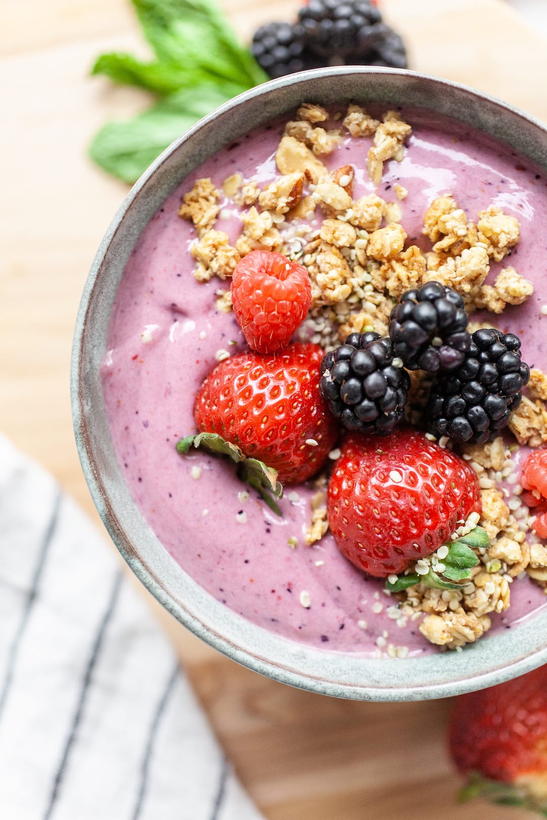 close up of a berry smoothie bowl topped with fresh strawberries, blackberries, and granola