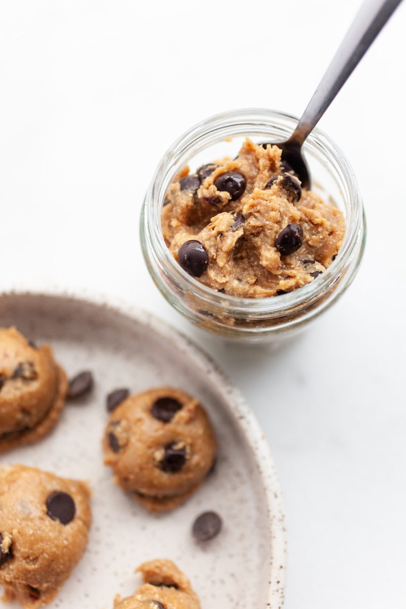 Vegan cookie dough in a jar with a spoon beside a plate with scoops of cookie dough