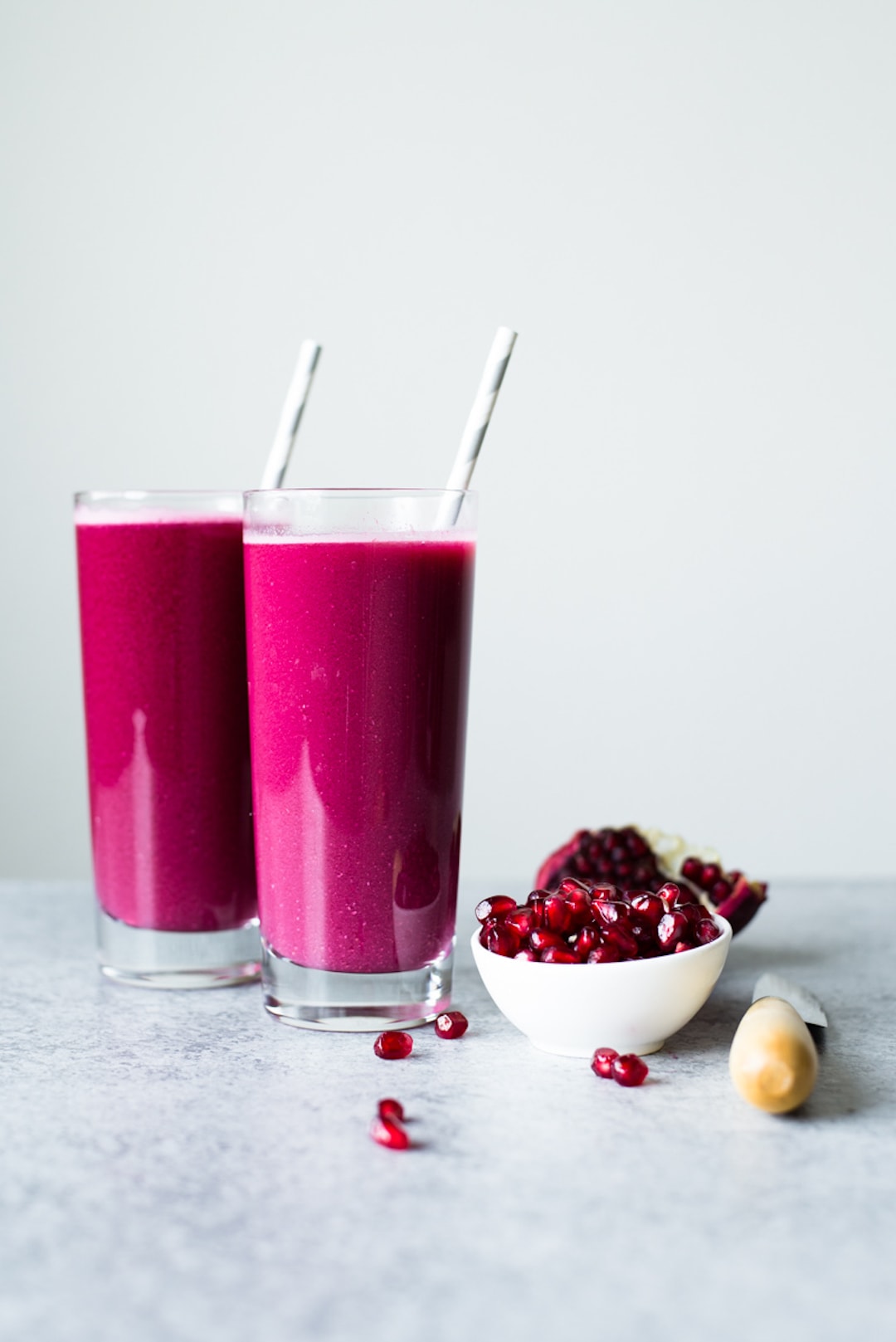 Two large glasses of pink juice with a bowl of pomegranate 