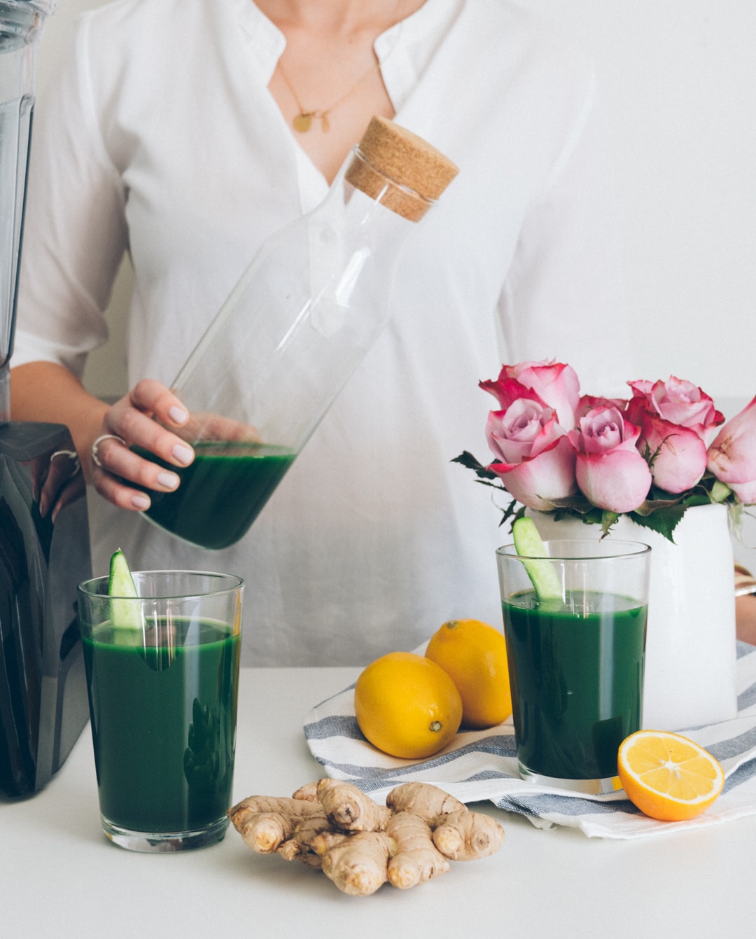 Woman with jug of dark green juice at a table with lemons