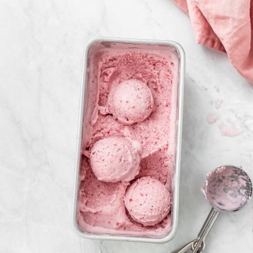 Pan of strawberry ice cream and an ice cream scoop on the side