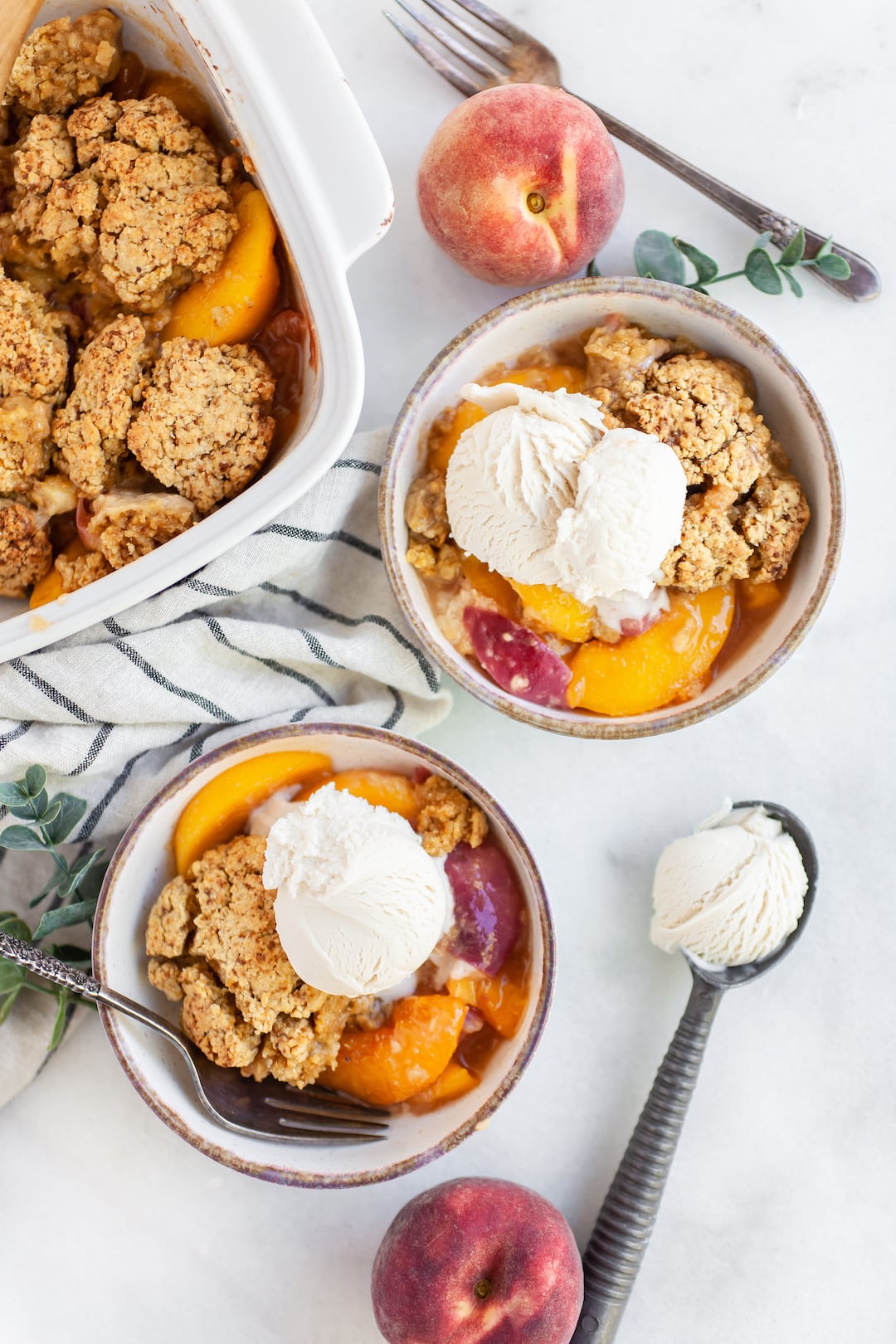 Two bowls of healthy peach cobbler with dairy free vanilla ice cream