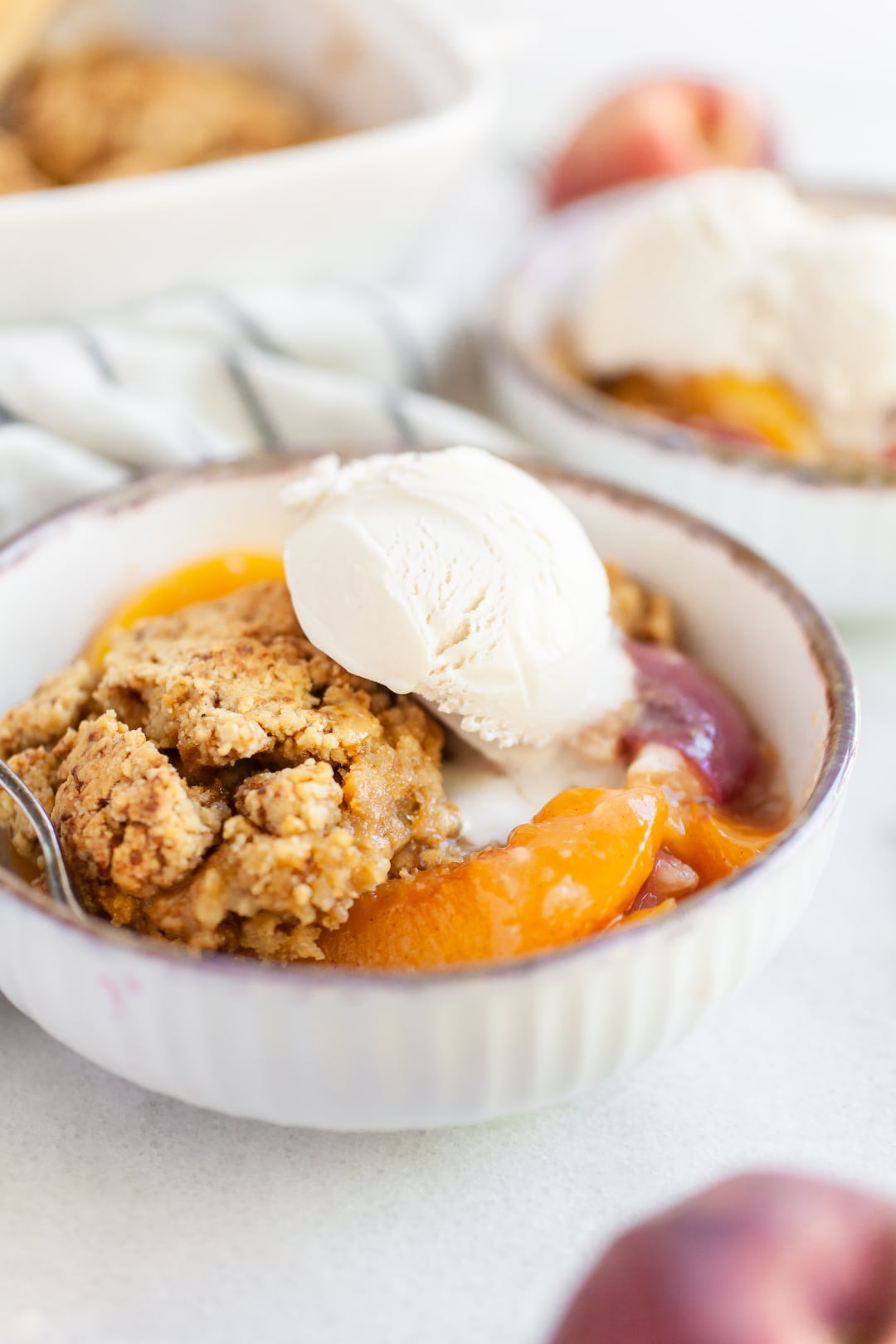 A bowl of healthy peach cobbler with dairy free vanilla ice cream