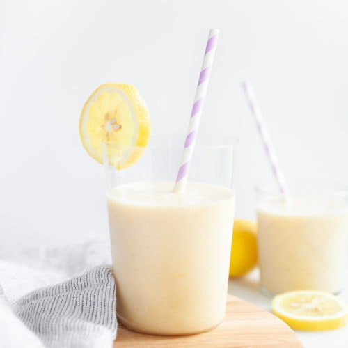 glass of banana peach lemon smoothie with lemon wedge and purple straw