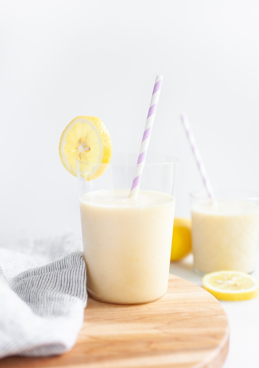 glass of banana peach lemon smoothie with lemon wedge and purple straw