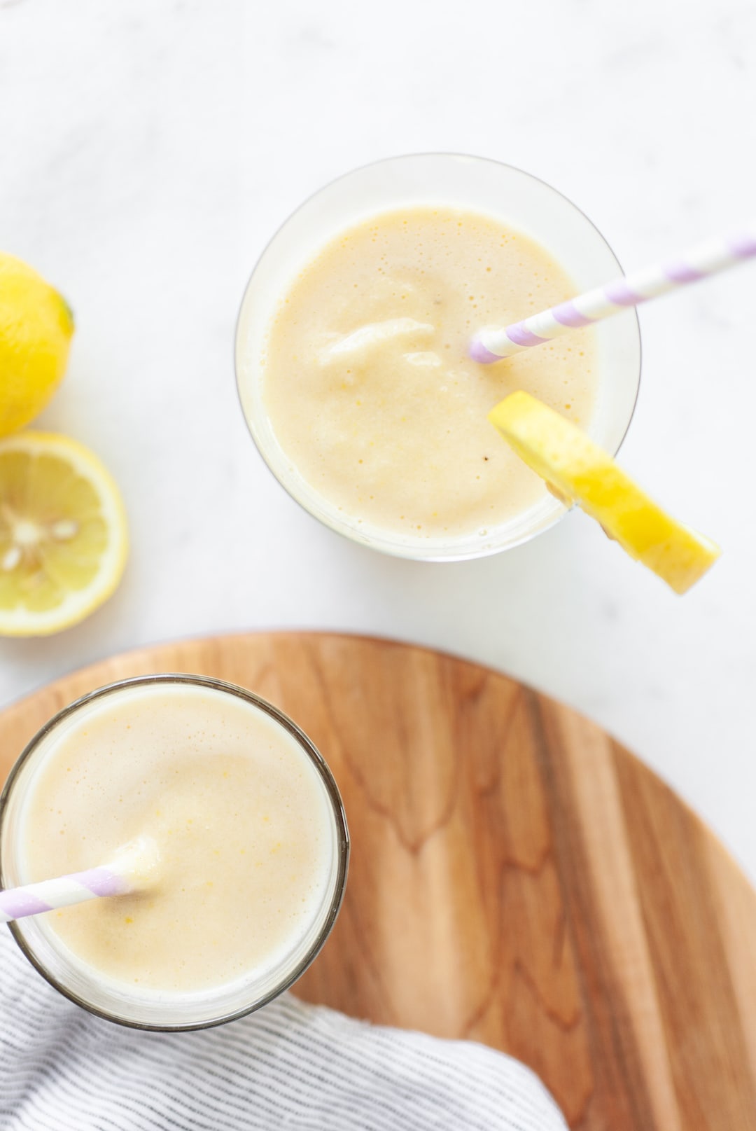 two glasses of lemon banana peach smoothie with lemon on the side