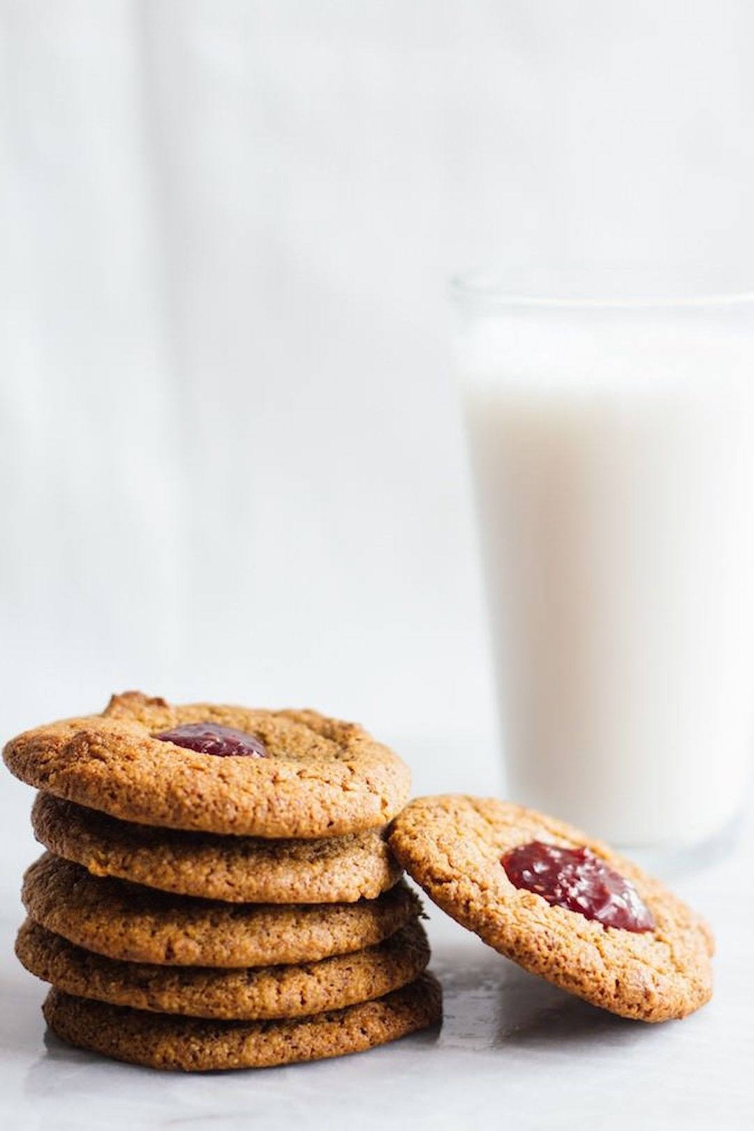 stacks of jam thumbprint cookies and a glass of milk