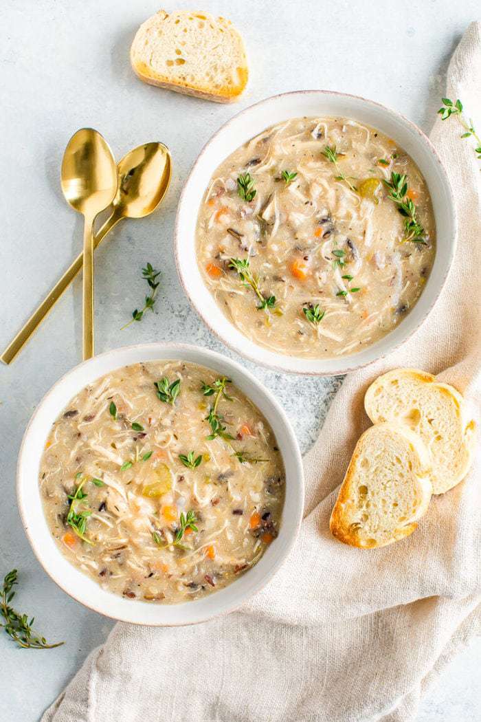 Slow cooker wild rice soup in two bowls with spoons and bread on the side
