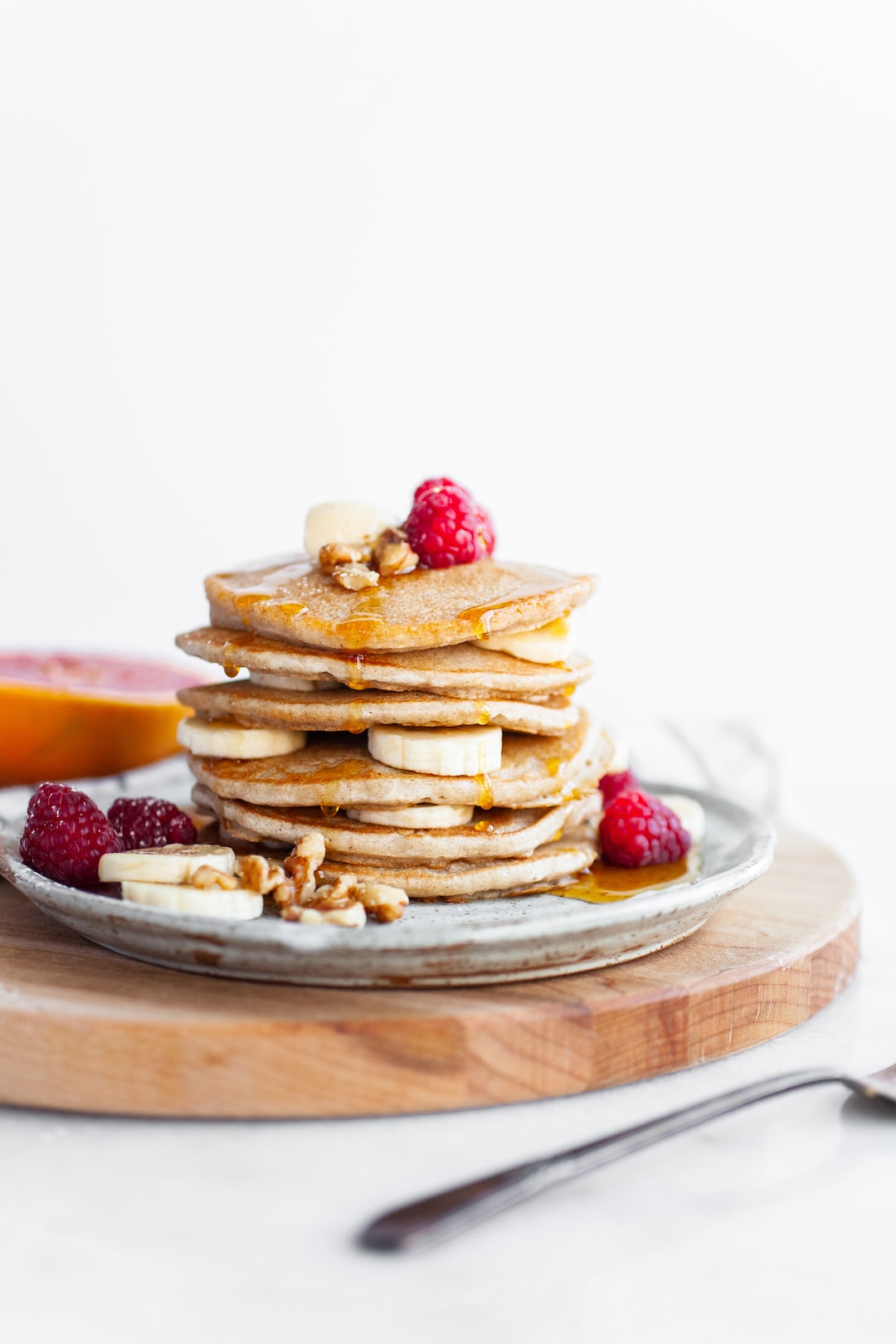 Perfect Vegan Buckwheat Pancakes stacked on a plate with raspberries and sliced banana