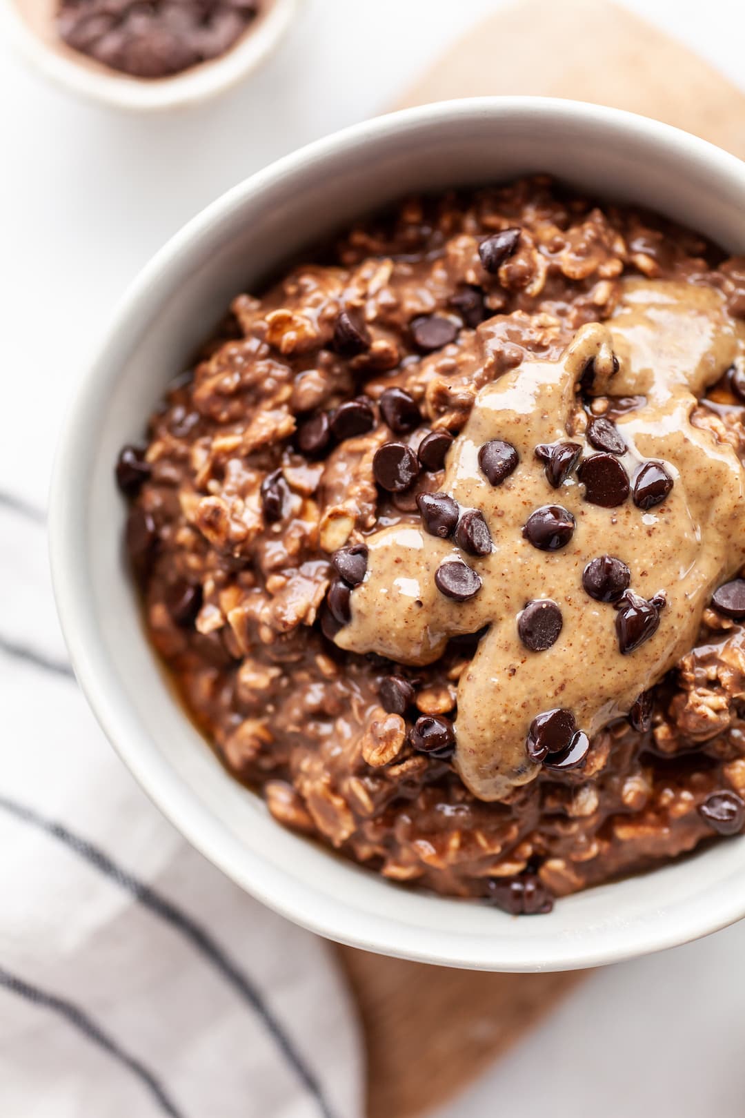 Close up of a white bowl filled with Healthy Chocolate Overnight Oats topped with almond butter and dark chocolate chips