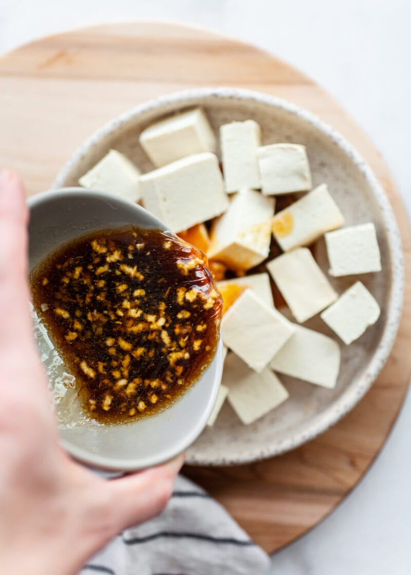 Pouring marinade over raw tofu in a dish for Crispy Air Fryer Tofu