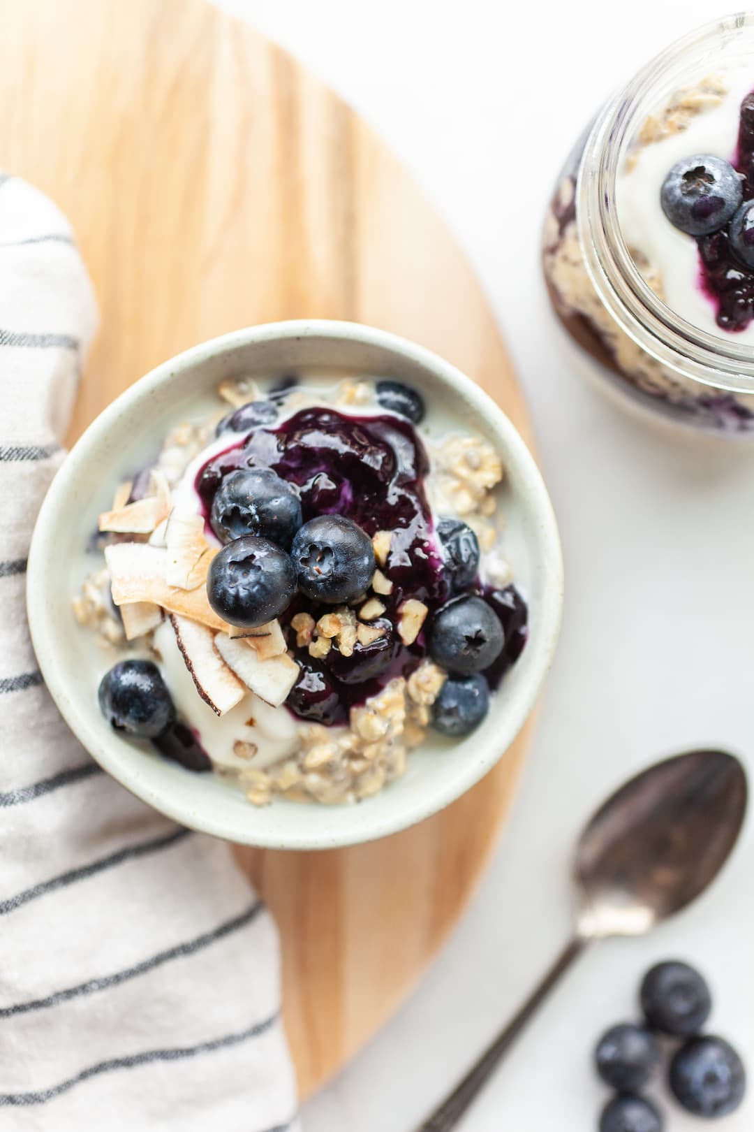 Bowl and jar of blueberry overnight oats on a wood tray with a white background