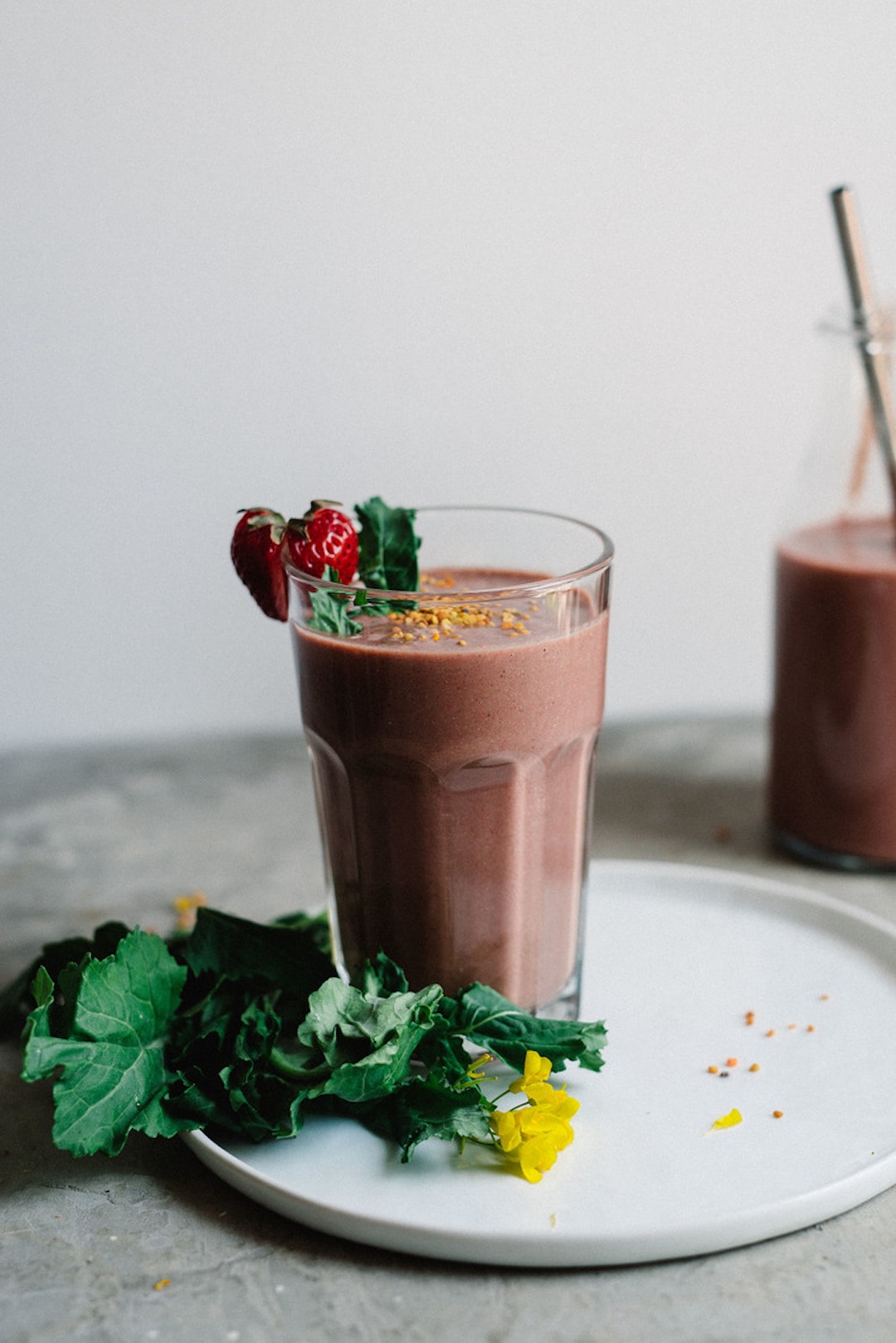 Bee pollen and berry smoothie in a glass with greens beside the glass