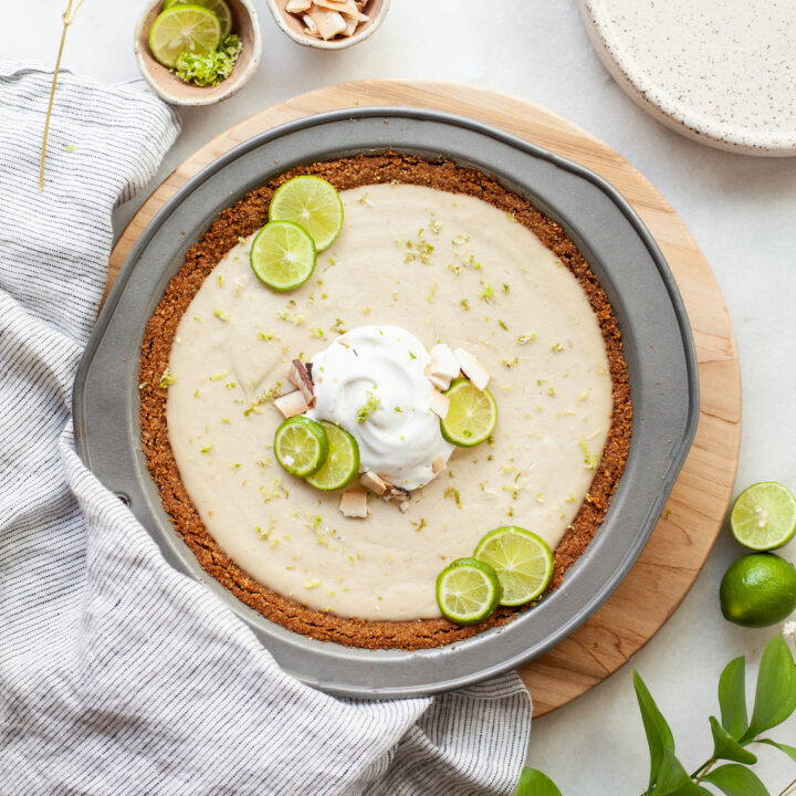 Vegan Key Lime Pie on a wood board topped with lime slices and whipped cram