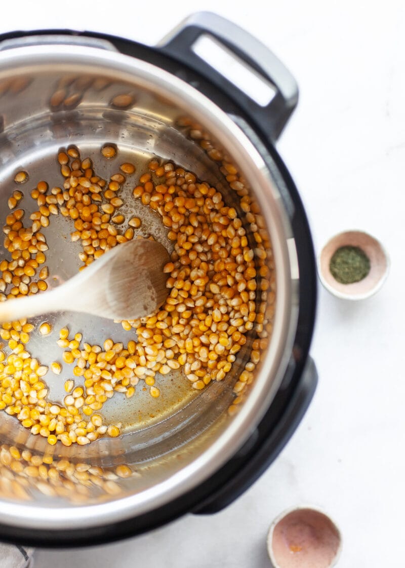Popcorn kernels in an instant pot with a wooden spoon