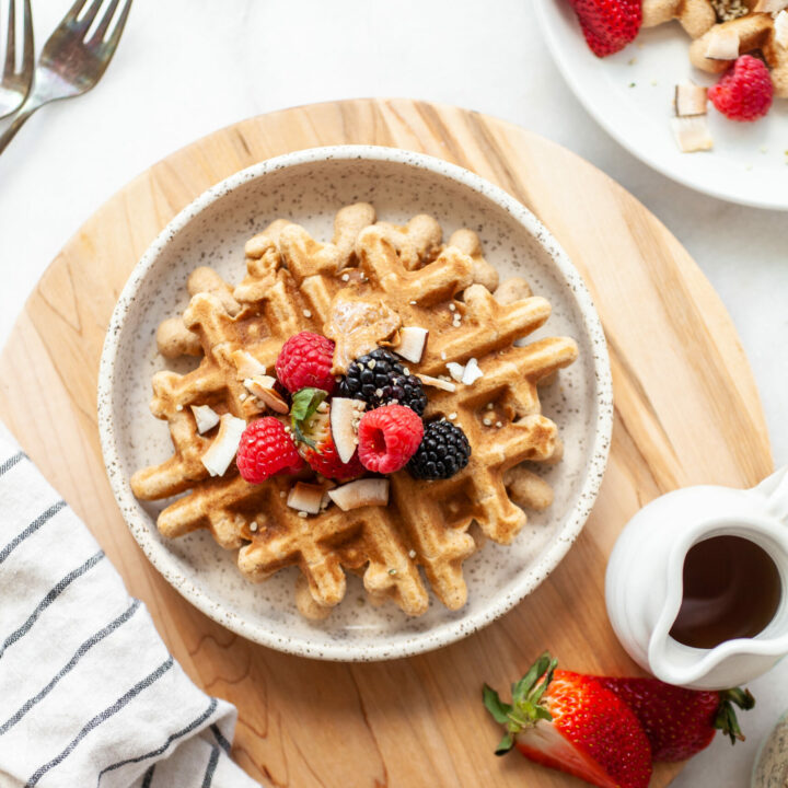 plate with Easy Coconut Flour Waffles on a wooden round board with maple syrup on the side