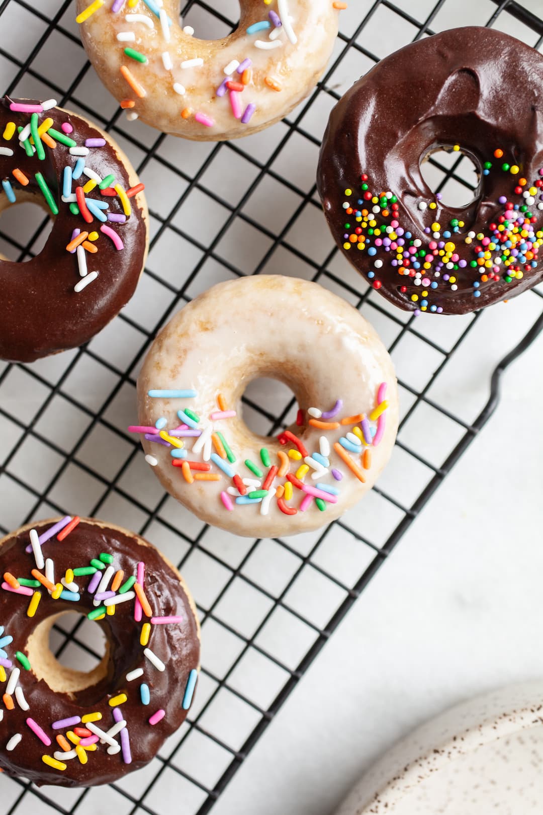 overhead view of Simple Vanilla Protein Donuts on a cooling rack iced with chocolate and vanilla glaze and rainbow sprinkles