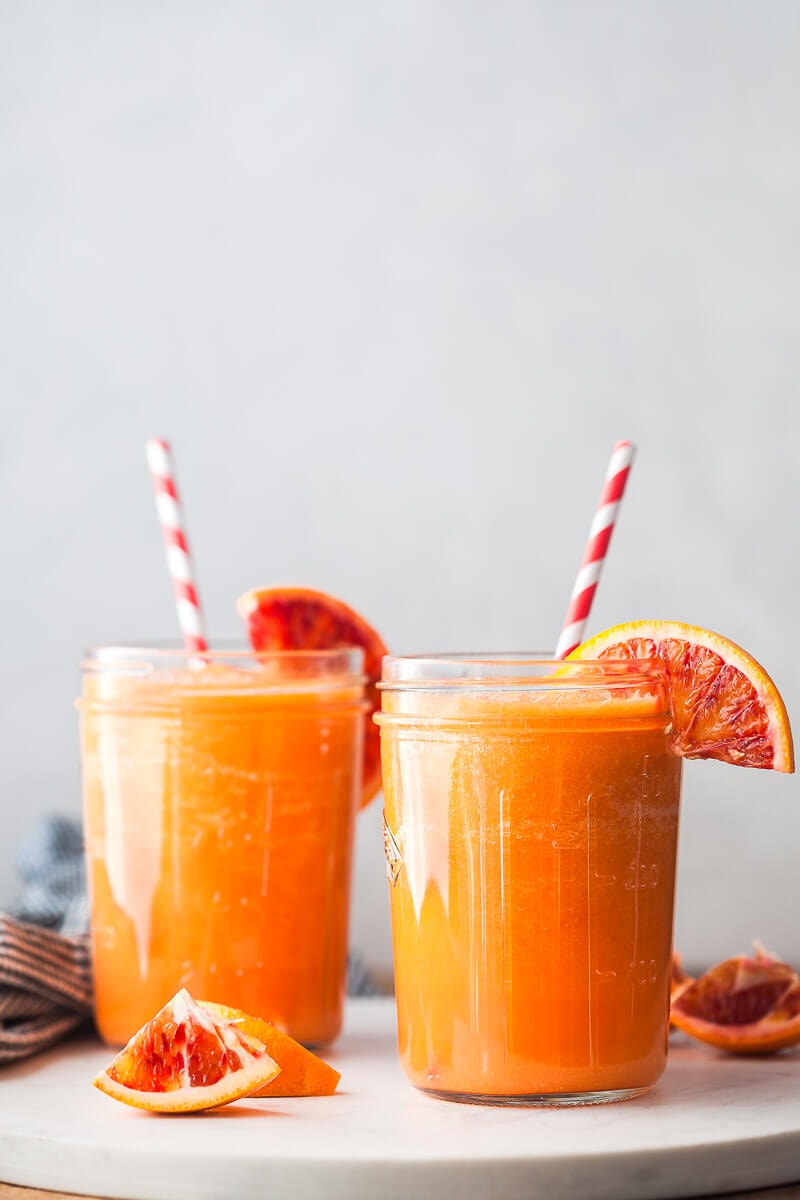 Two apple carrot orange smoothies in glass jars with straws and orange slices to garnish