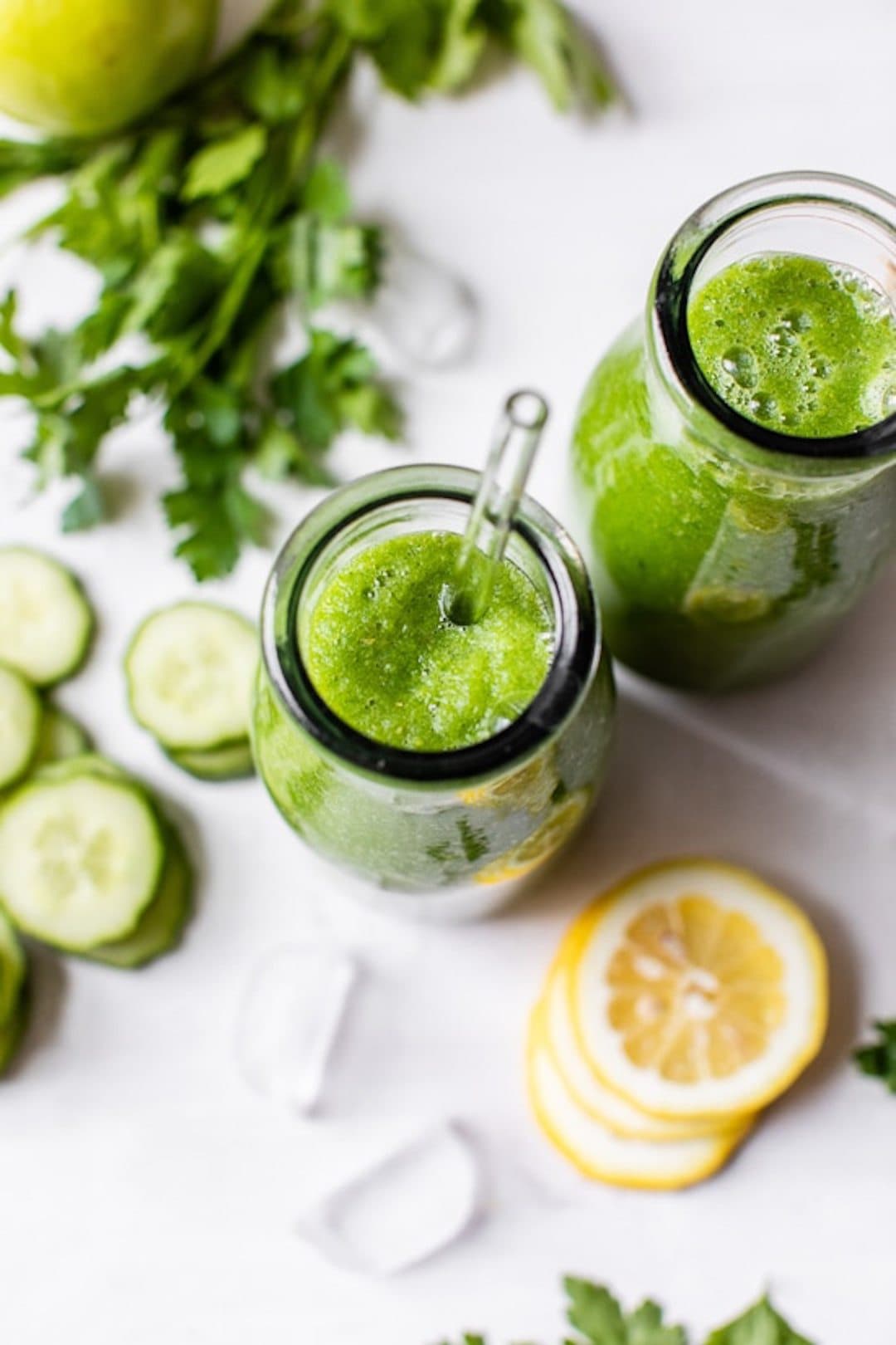 two glasses filled with cucumber smoothie with cucumber slices and lemon slices on the side