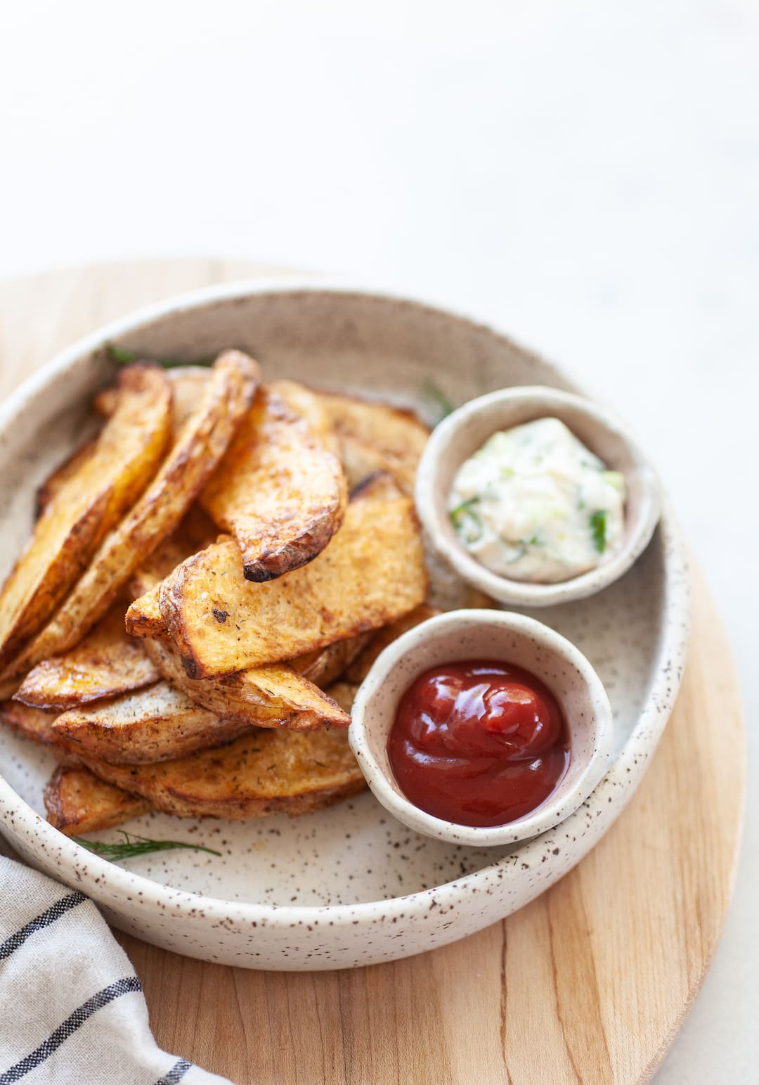 Plate of air fried potato wedges with two ramekins of ketchup and aioli dip