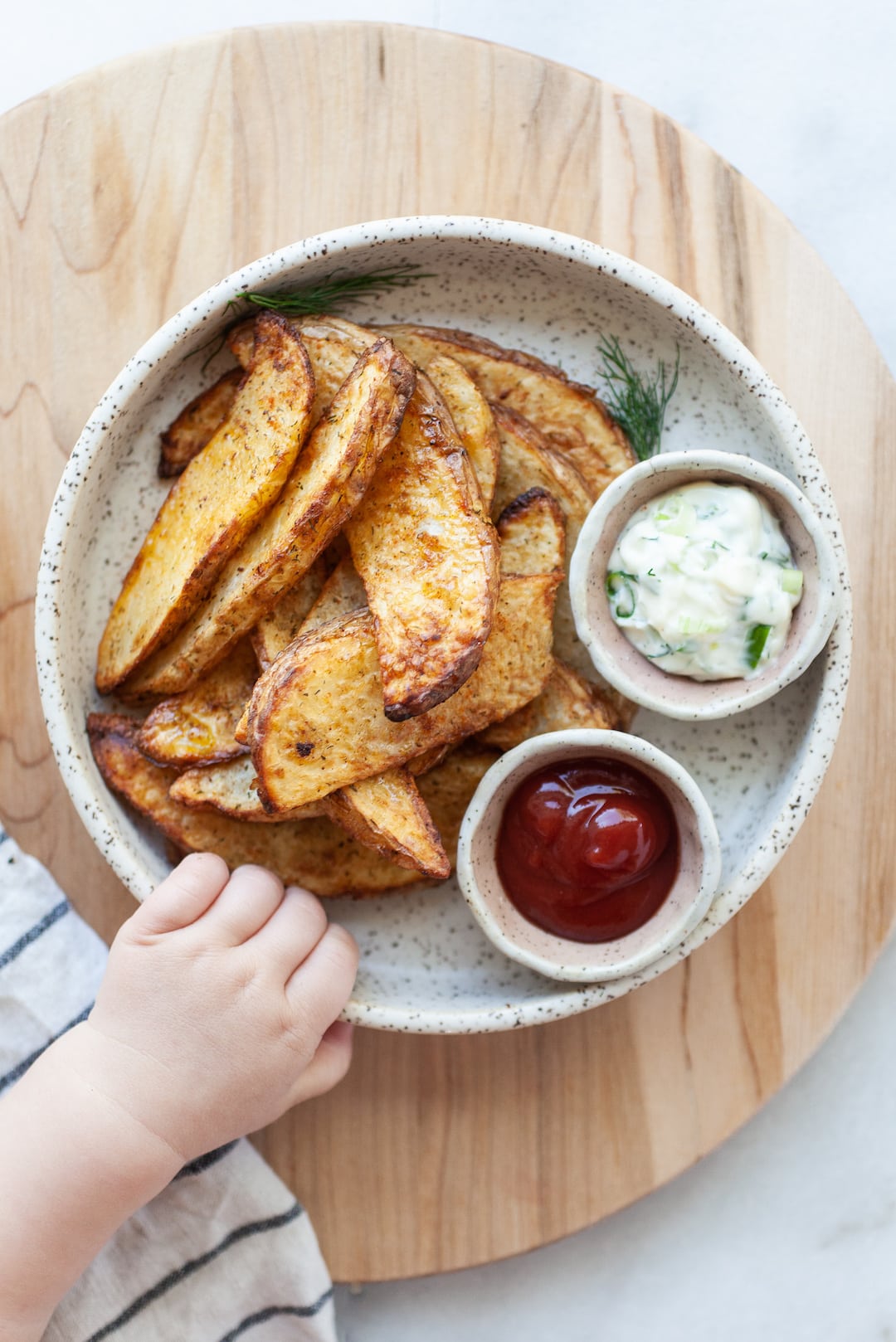 Air Fried Potato Wedges on a plate with a small Childs hand reaching for the plate
