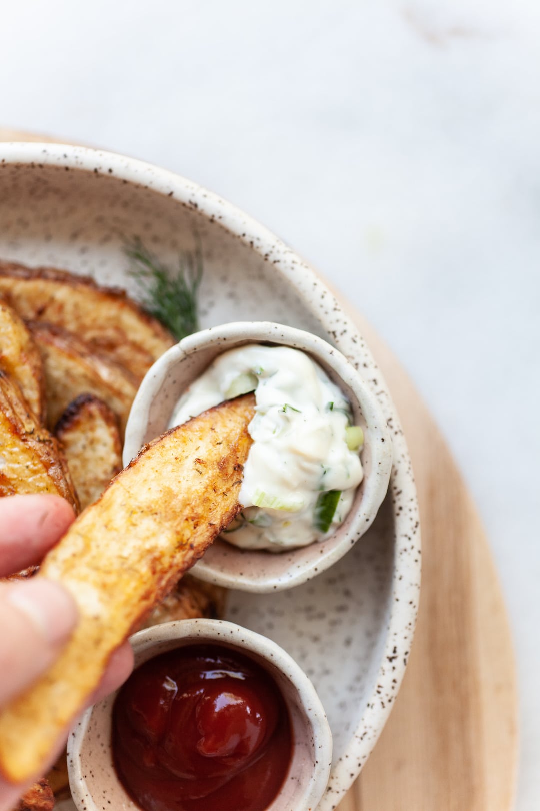 dipping an air fried potato wedge into a small bowl of aioli dip