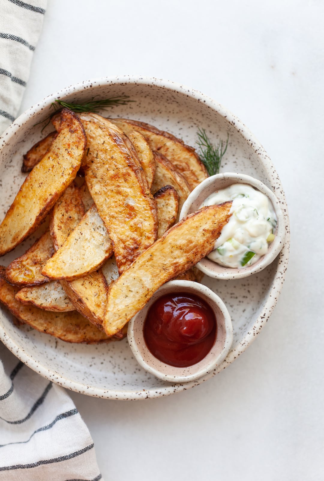 Air Fried Potato Wedges on a plate with one wedge dipped into a small bowl of aioli
