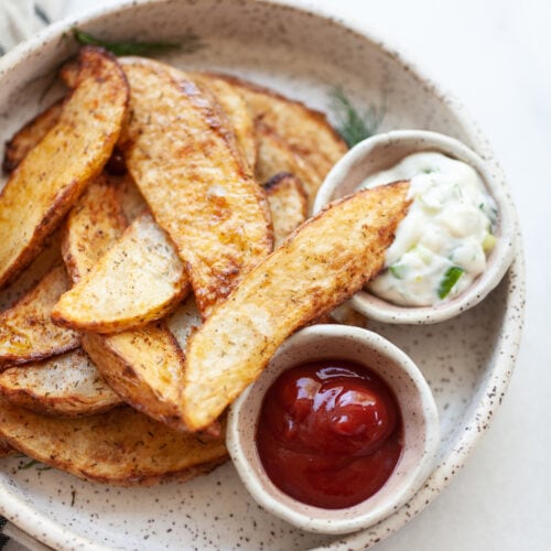 Air Fried Potato Wedges on a plate with one wedge dipped into a small bowl of aioli