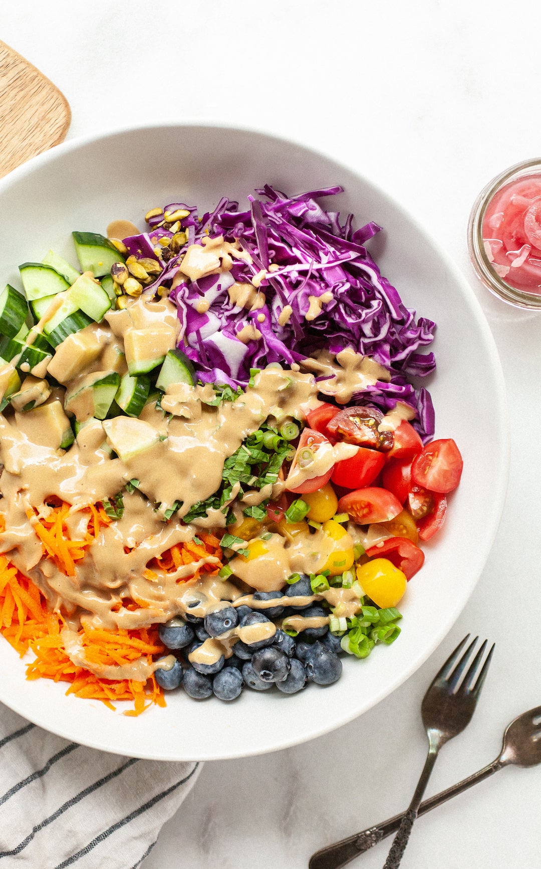 rainbow salad in a large white bowl drizzled with tahini balsamic dressing