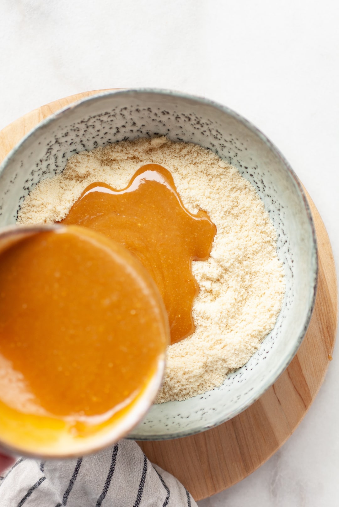 Almond flour in a bowl with peanut butter mixture being poured into the bowl