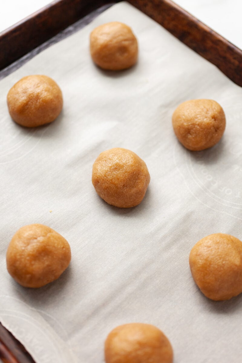 raw almond flour peanut butter cookie balls on a baking tray covered with parchment paper