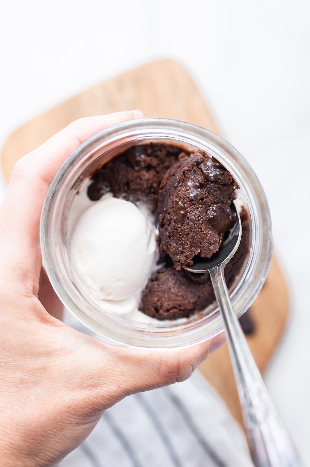 hand holding a jar of vegan mug brownie with a spoon in the jar and a scoop of vanilla vegan ice cream