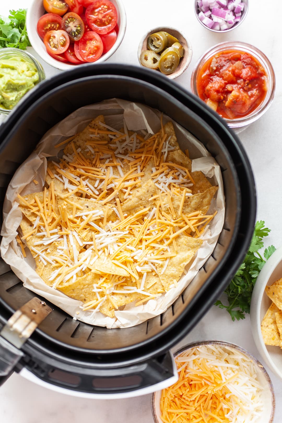 tortilla chips topped with shredded cheese in an air fryer basket