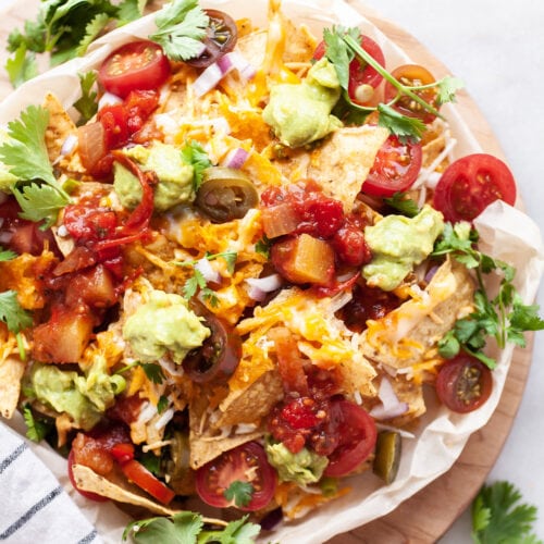 Air Fryer Nachos on a plate covered with tomatoes, cilantro, onion, jalapeños, cheese, and guacamole
