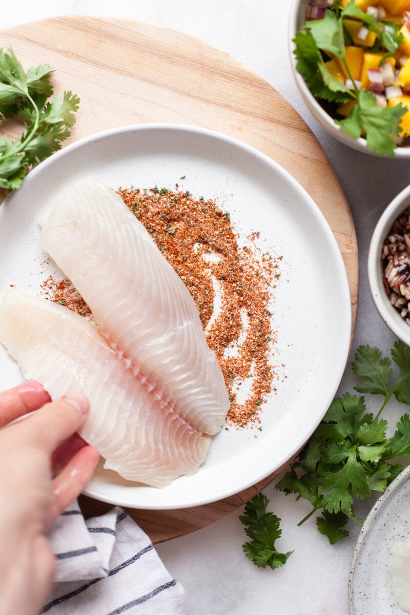 tilapia filets being dipped in a seasoning mixture on a plate