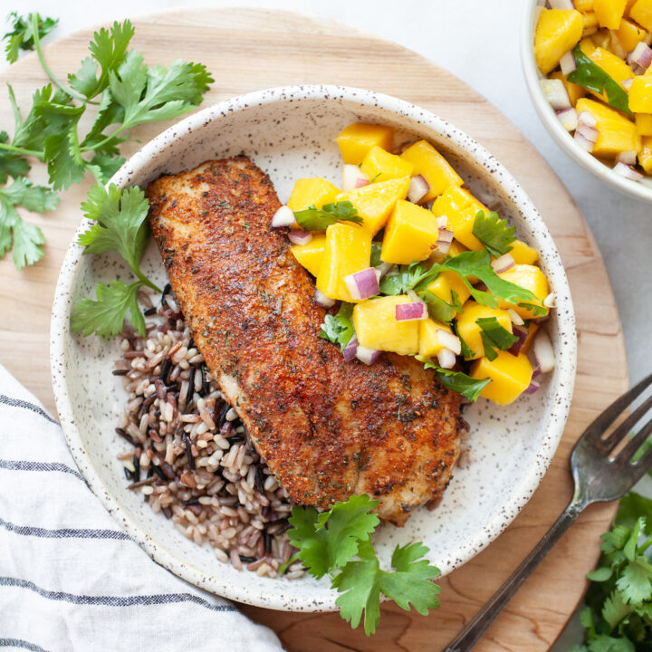 Plate of Air Fryer Tilapia on a bed of wild rice with mango salsa and cilantro on the side