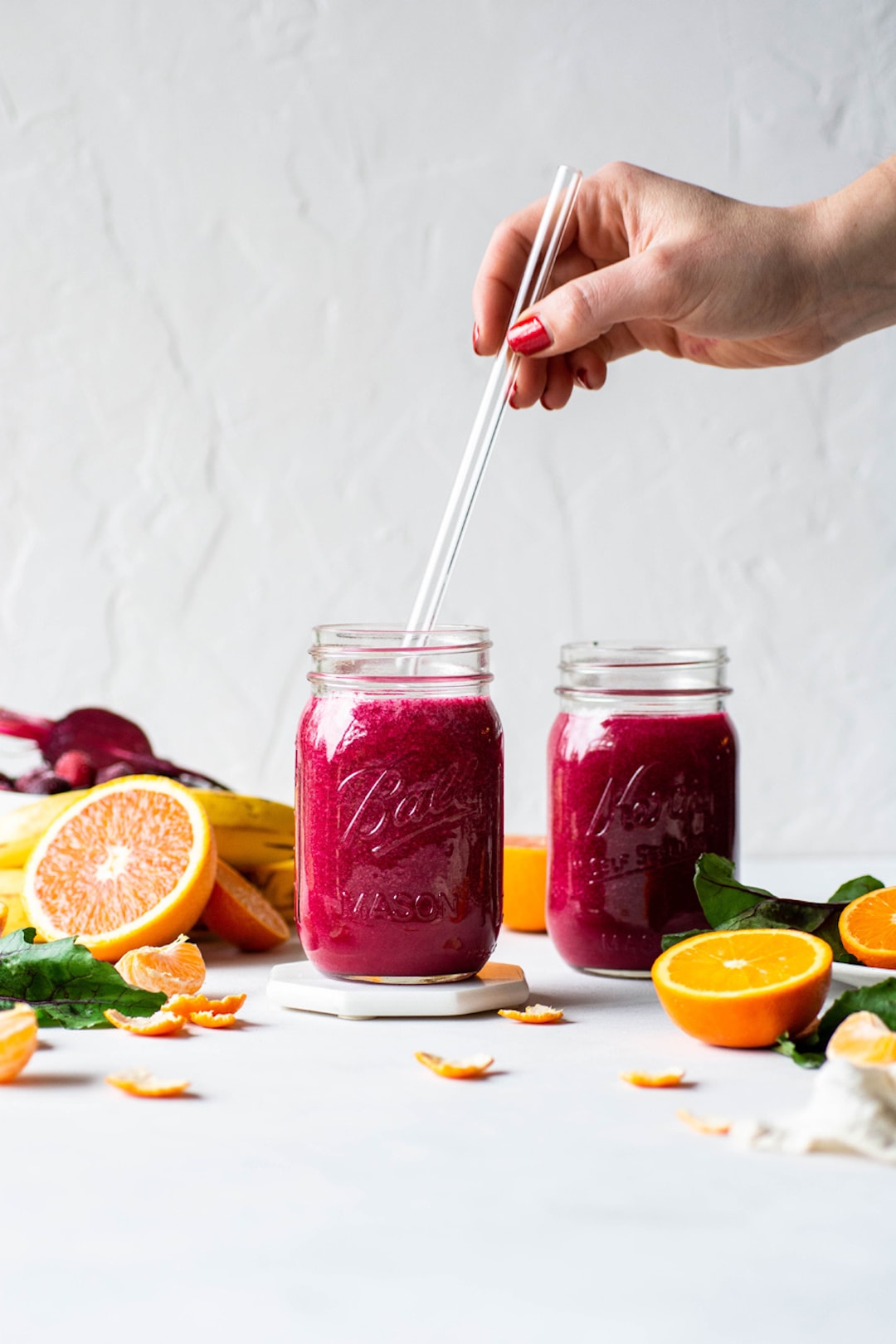 beet and berry smoothies in two glass jars with oranges on the side