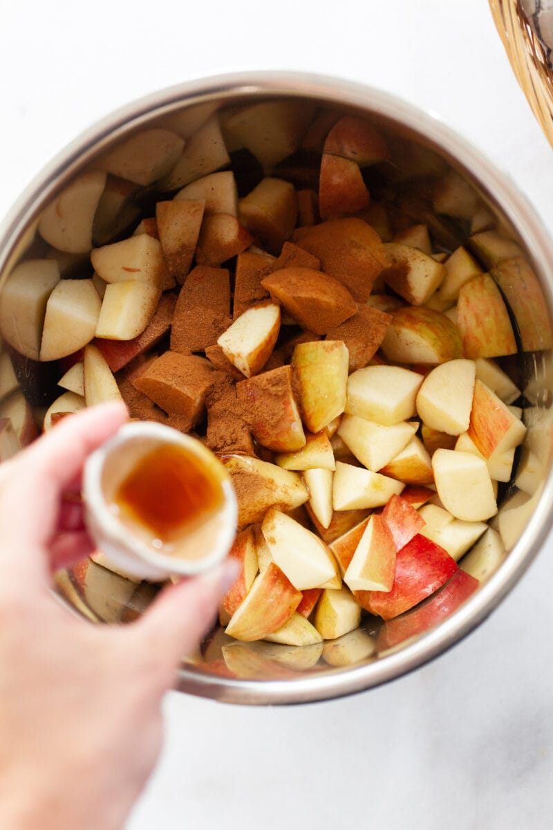 pouring maple syrup onto diced apples covered in cinnamon in an instant pot
