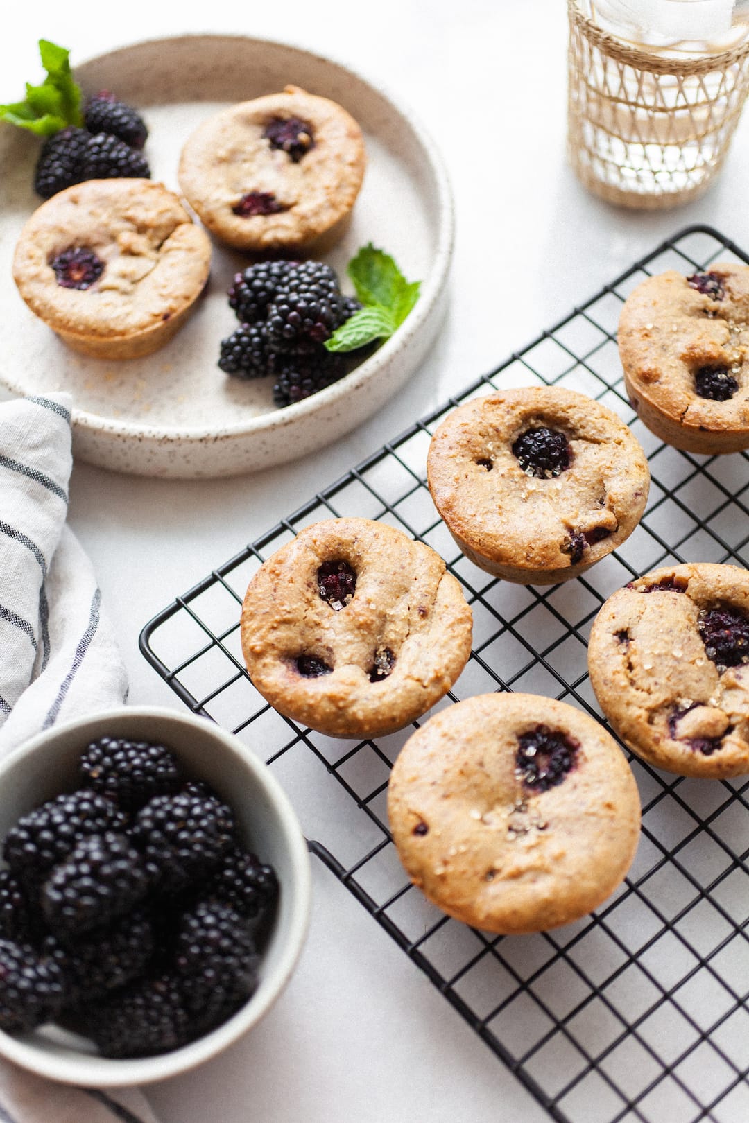 Vegan Blackberry Muffins on a cooling rack beside a bowl of blackberries