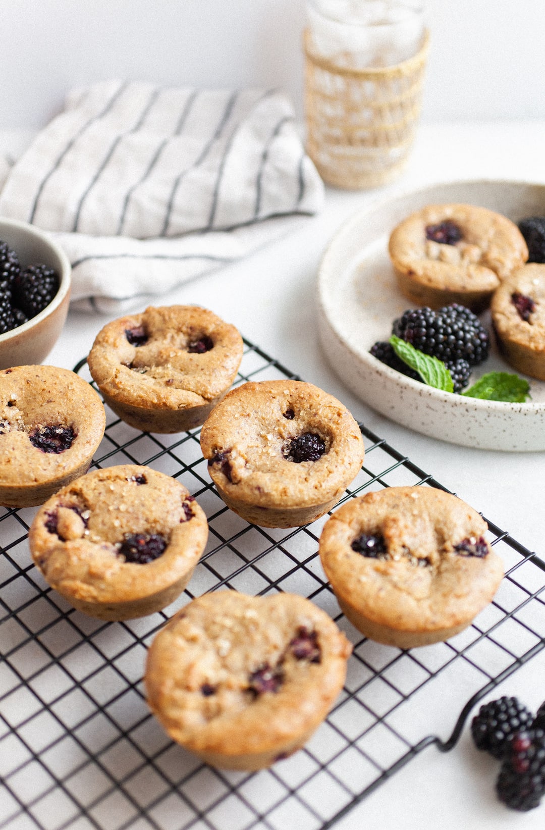 Vegan Blackberry Muffins on a cooling rack beside a bowl of blackberries