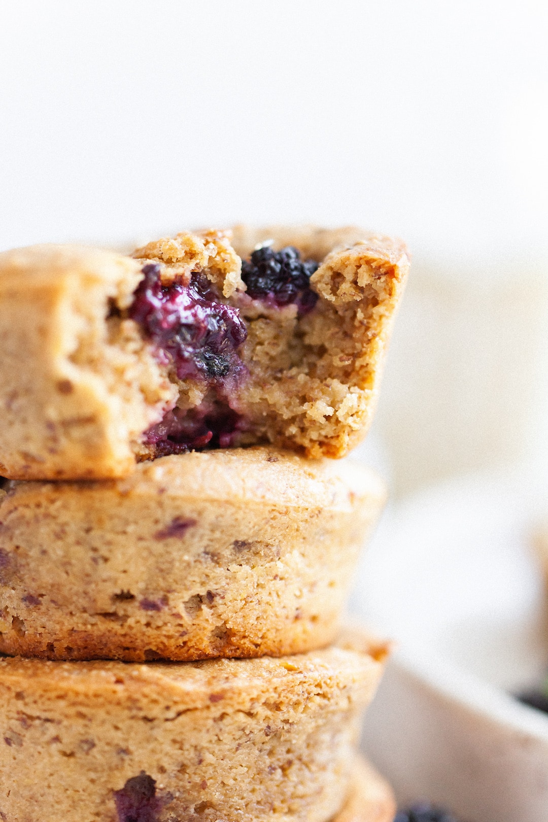 Close up of a stack of vegan blackberry muffins with the top muffin with a bite taken out of it