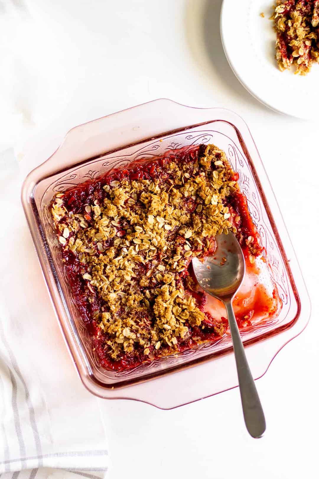 glass dish filled with strawberry crumble and a silver spoon