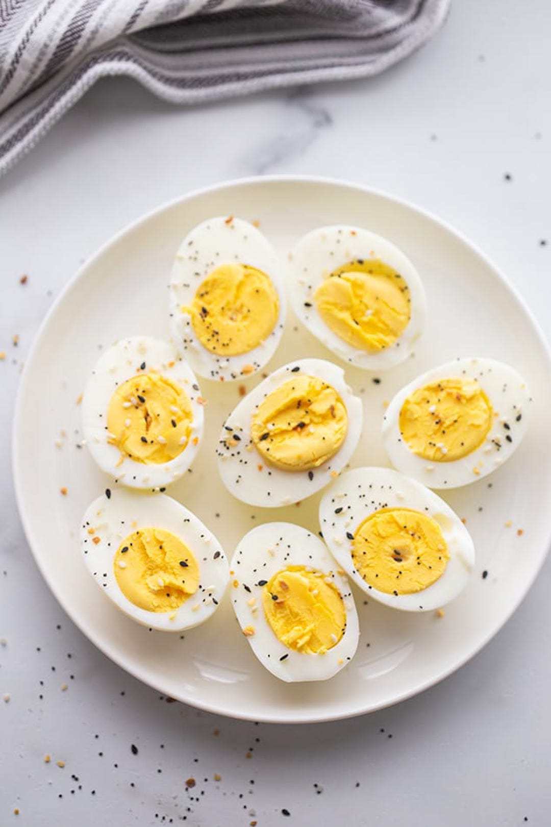 image of a white plate topped with air fryer boiled eggs cut in half sprinkled with sesame seeds