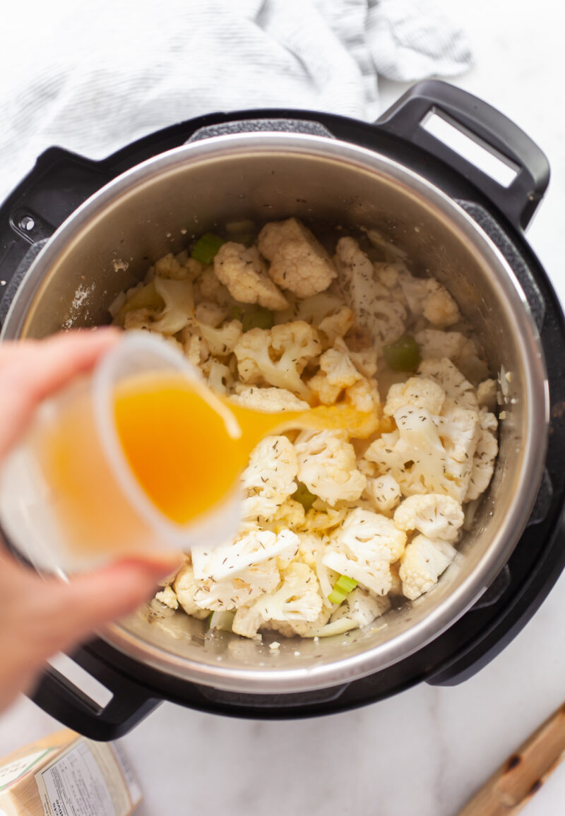 image of cauliflower in an instant pot with a hand pouring in broth