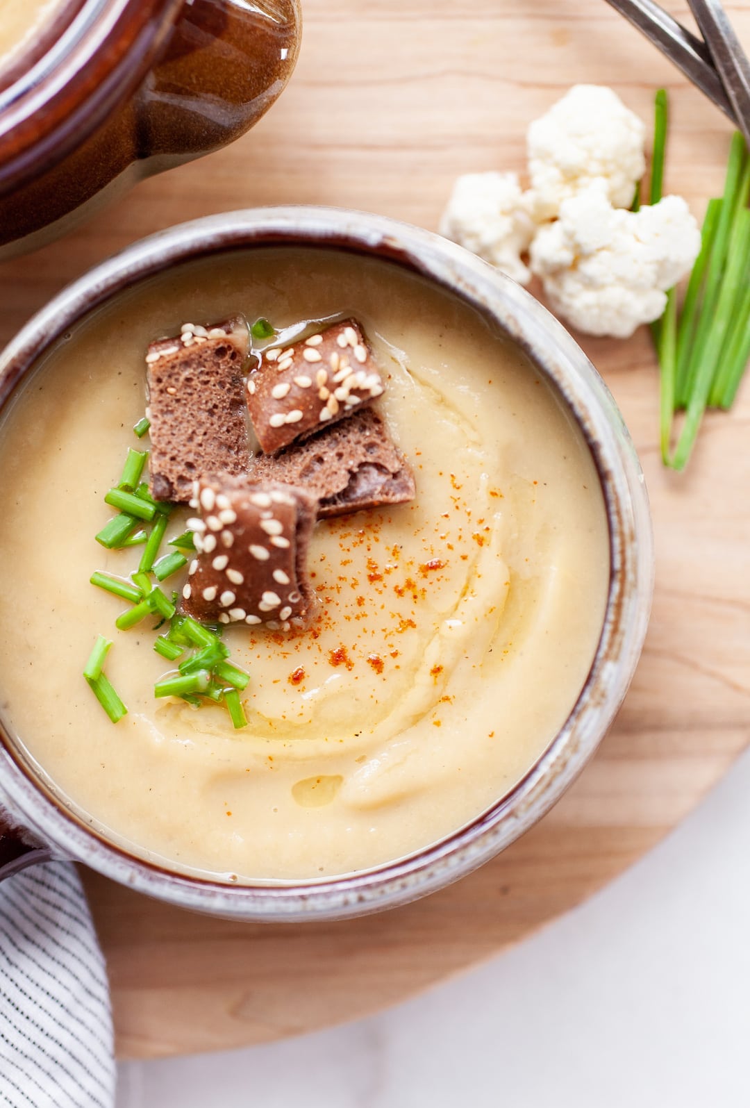 image of instant pot cauliflower soup in a rustic bowl with croutons and chives on a wood board