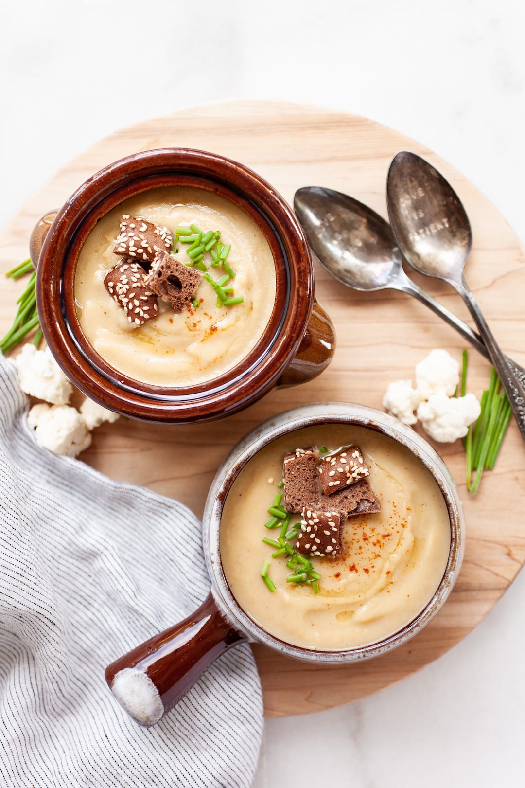 image of two bowls of instant pot cauliflower soup in a rustic bowl with croutons and chives on a wood board